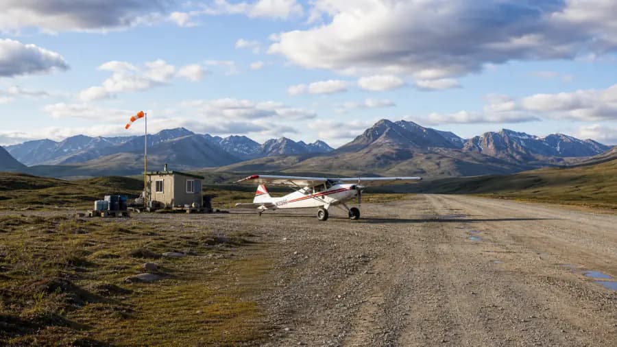 Utility aircraft at a remote gravel airstrip in mountain terrain